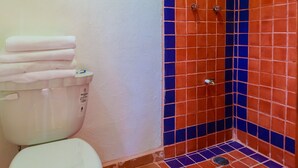 A bathroom with a white toilet, a stack of white towels, and a shower with orange and blue tiles. - One Bedroom Suite, Serene, Pool, Gardens, Rooftop Terrace with Views (Isla Mujeres)