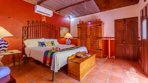 A room with a bed, a wooden chest, a lamp, a wall-mounted air conditioner, and a door. - One Bedroom Suite, Serene, Pool, Gardens, Rooftop Terrace with Views (Isla Mujeres)