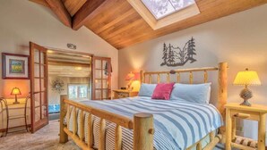 A cozy bedroom with a wooden bed, a skylight, a nightstand with a lamp, and a wall-mounted artwork. - AC, Luxurious, vaulted ceilings, great home for couples, dogs allowed (Sunriver)