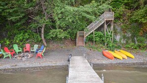 Eine Holzsteg führt zu einer kleinen Holztreppe, mit bunten Adirondack-Stühlen und Kanus am Ufer.