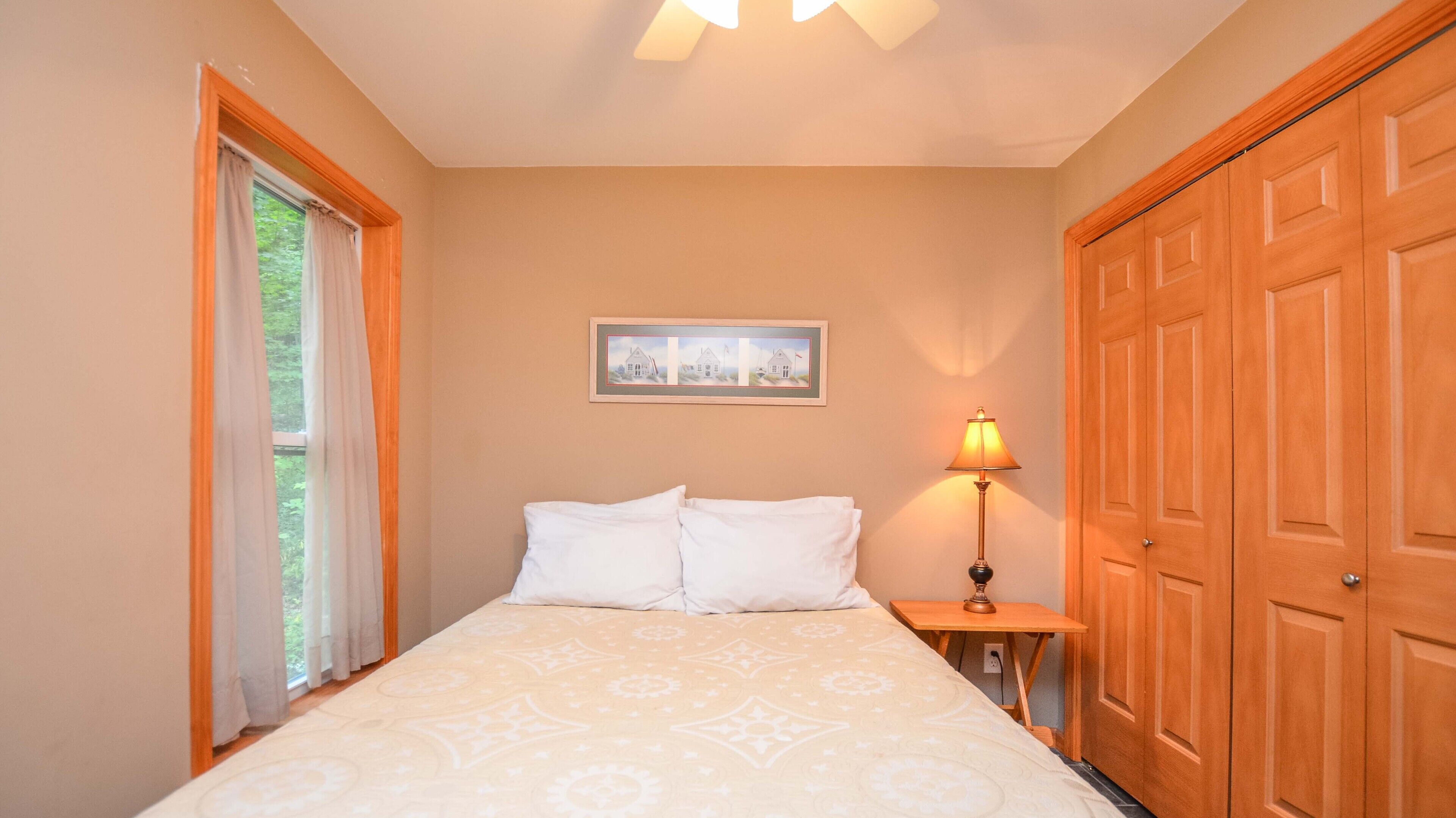 A bedroom with a bed, a nightstand, a lamp, a framed picture on the wall, and a wooden door.