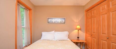 A bedroom with a bed, a nightstand, a lamp, a framed picture on the wall, and a wooden door.