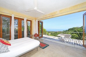 A bedroom with a bed, a ceiling fan, a view of the ocean, and a balcony with a chair and table. - 3 Bedroom, 4 Bath, 30 ft. Soaring Palapa, Spectacular Ocean Views, 40 foot pool (Sayulita)