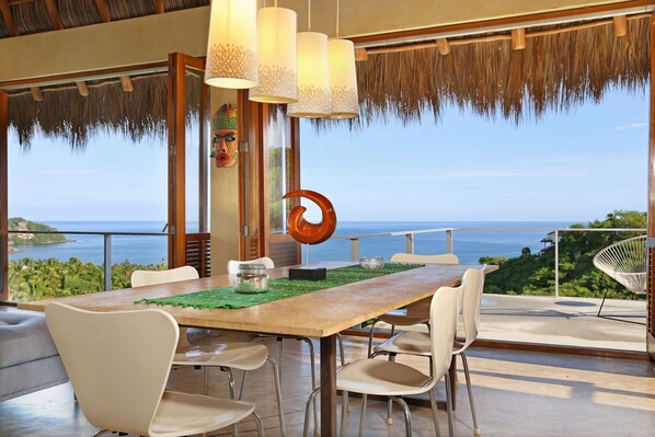 A dining area with a wooden table, white chairs, and a view of the sea.