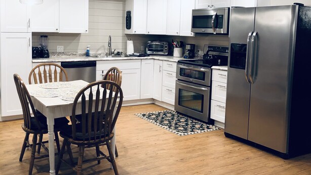 Een moderne keuken met witte kasten, roestvrijstalen apparatuur, een eettafel met stoelen en een vloerkleed met dessin.