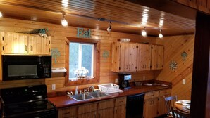 Una cocina con gabinetes de madera, microondas, estufa, lavabo y ventana con vista a árboles.