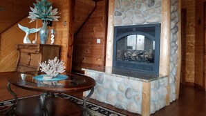 Una habitación acogedora con chimenea de piedra, paredes de madera y una mesa de vidrio con adornos.