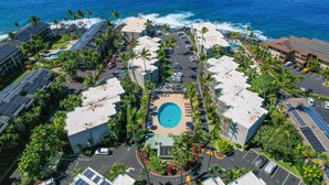 Vista aérea de un complejo turístico con una piscina central, rodeado de edificios y palmeras, con vistas al océano.