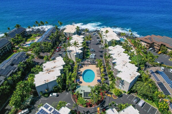 An aerial view of a resort with a central swimming pool, surrounded by buildings and palm trees, overlooking the ocean. - Spectacular Ocean Front Condo: 2 bedroom - 2 bath (Kailua-Kona)