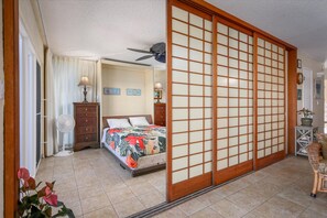 Un dormitorio con cama, ventilador de techo, panel corredero shoji, cómoda y mesita de noche con lámpara.