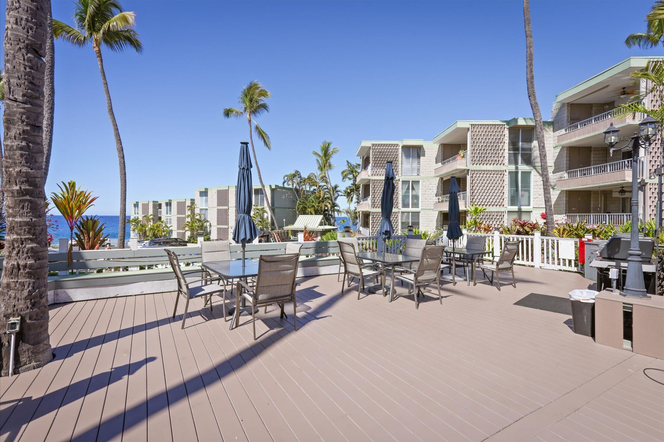 A resort deck with outdoor seating, palm trees, and a view of the ocean.