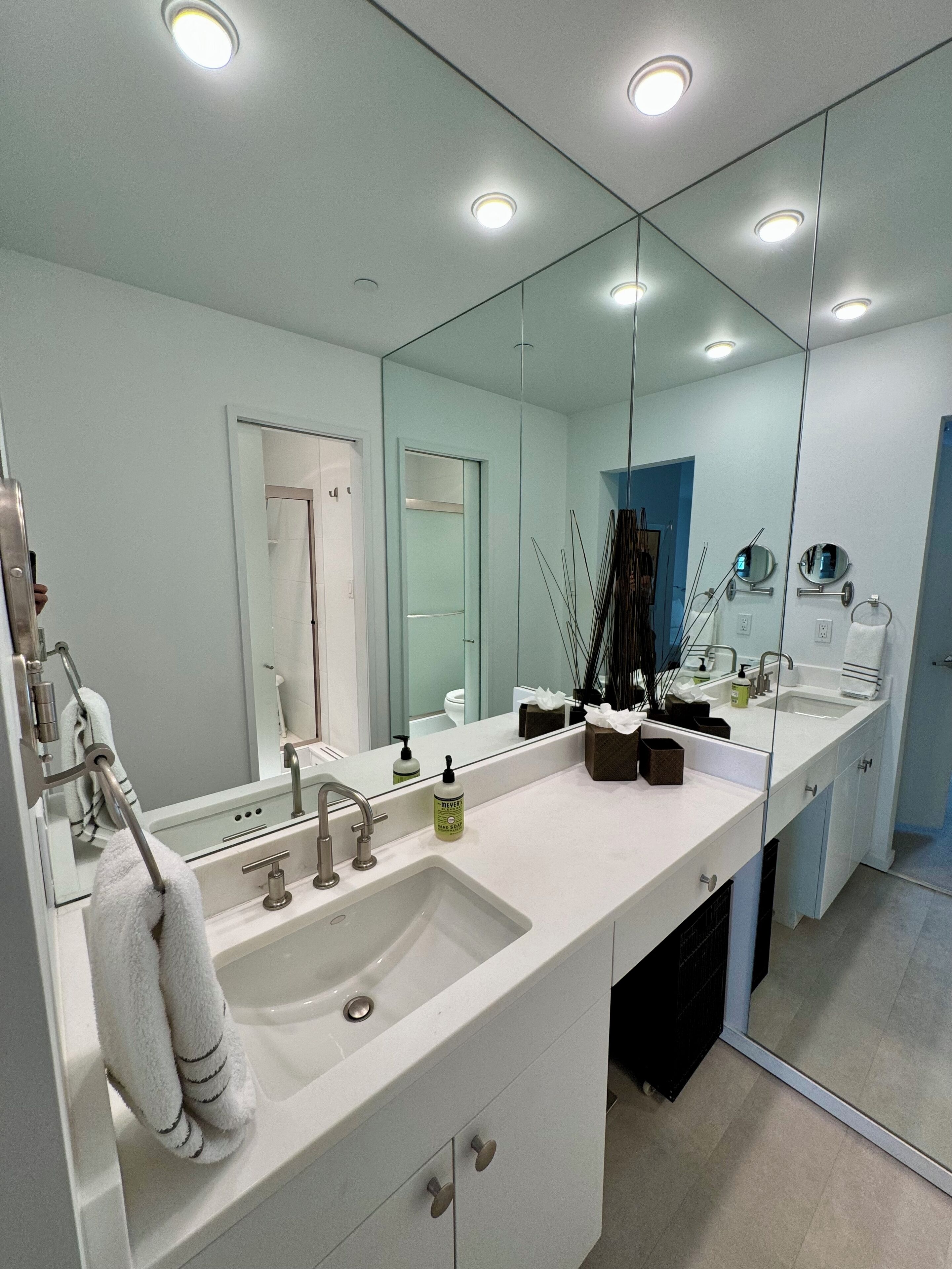 A modern bathroom with a large mirror, white sink, and a towel rack.
