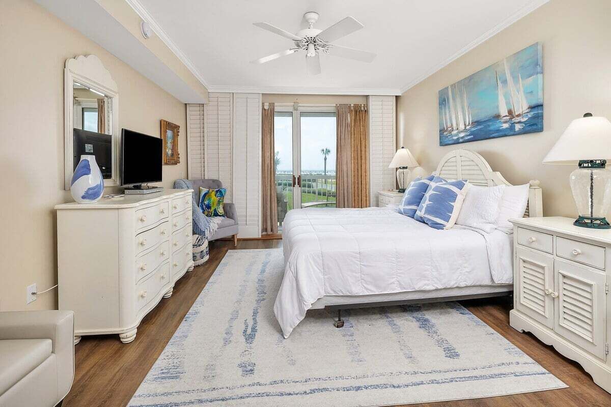 A bedroom with a bed, a dresser, a television, a painting, and a view through the window.