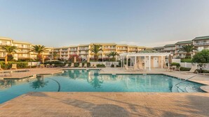 Un espace piscine d’hôtel offrant une vue dégagée sur la piscine, des chaises longues et un espace salon abrité.