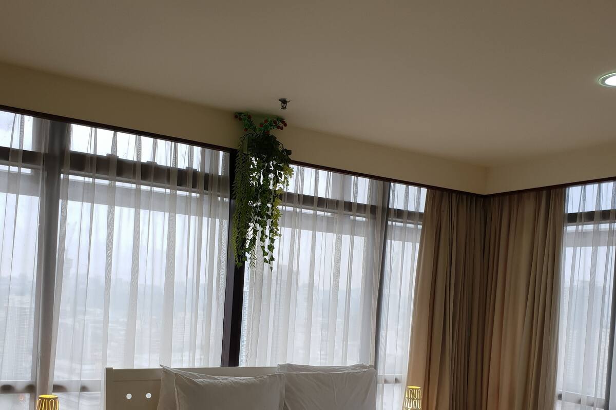 A modern bedroom with a large bed, a bedside table with a lamp, and a view through large windows.