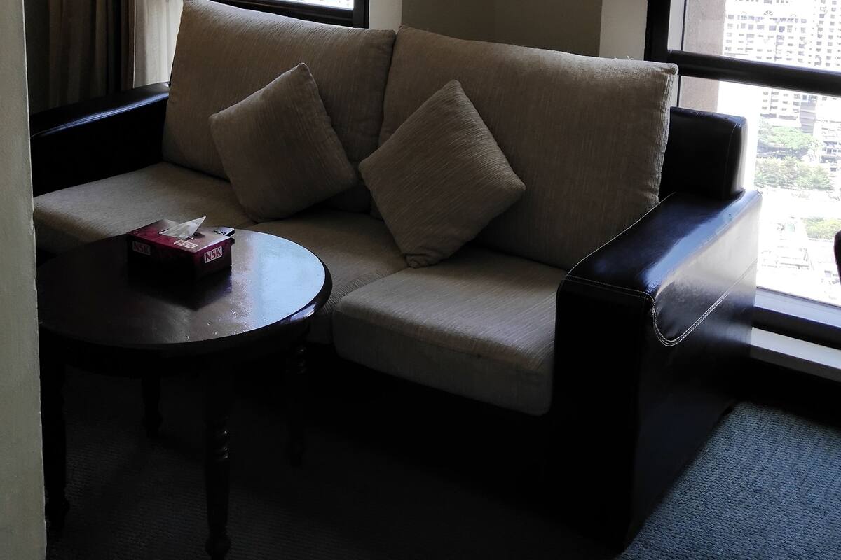 A hotel room with a sofa, a small round table, and a window with a city view.