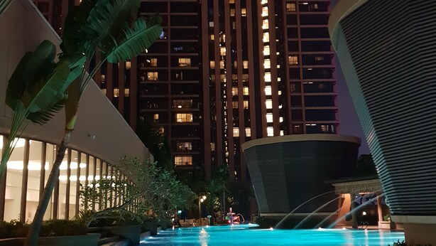 A nighttime pool area with a view of a tall building in the background. - Residency Suites At Times Square (Kuala Lumpur)