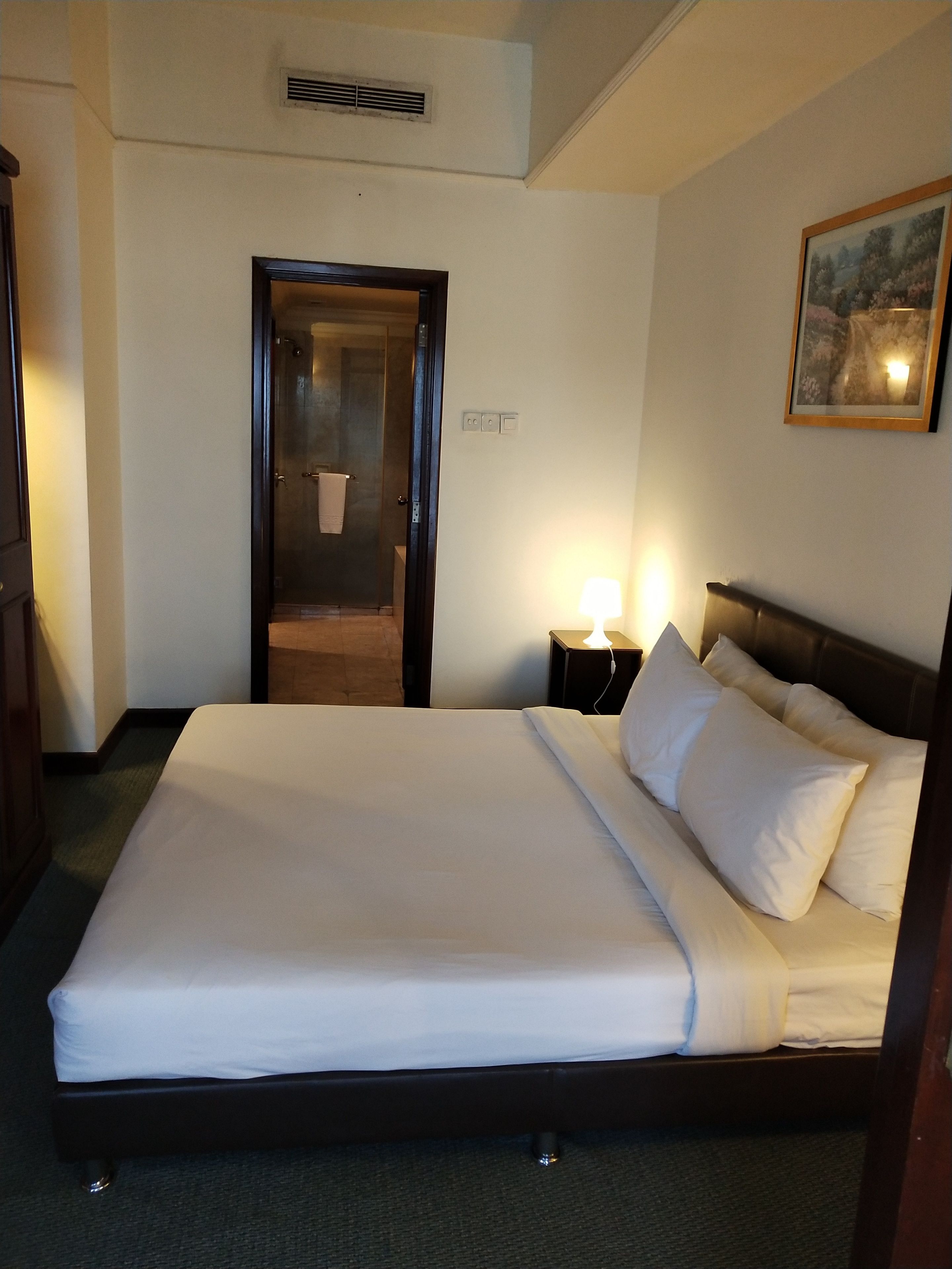 Ett hotellrum med en stor säng, en sänglampa, en dörr som leder till badrummet och en inramad tavla på väggen.