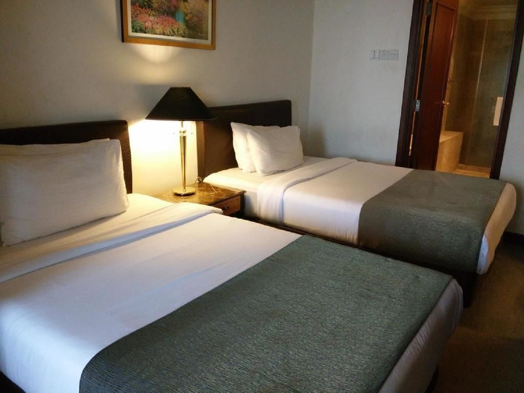 A hotel room with two beds, a nightstand with a lamp, and a door leading to a bathroom.