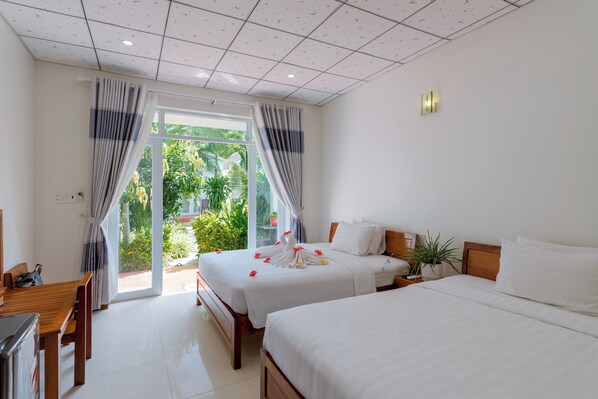 Ein Hotelzimmer mit zwei Betten, einem Holztisch, einem Fernseher und Blick auf Grün hinter dem Fenster.