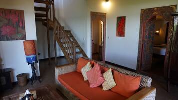 Un salón con sofá de mimbre, una escalera de madera y un espejo decorativo.