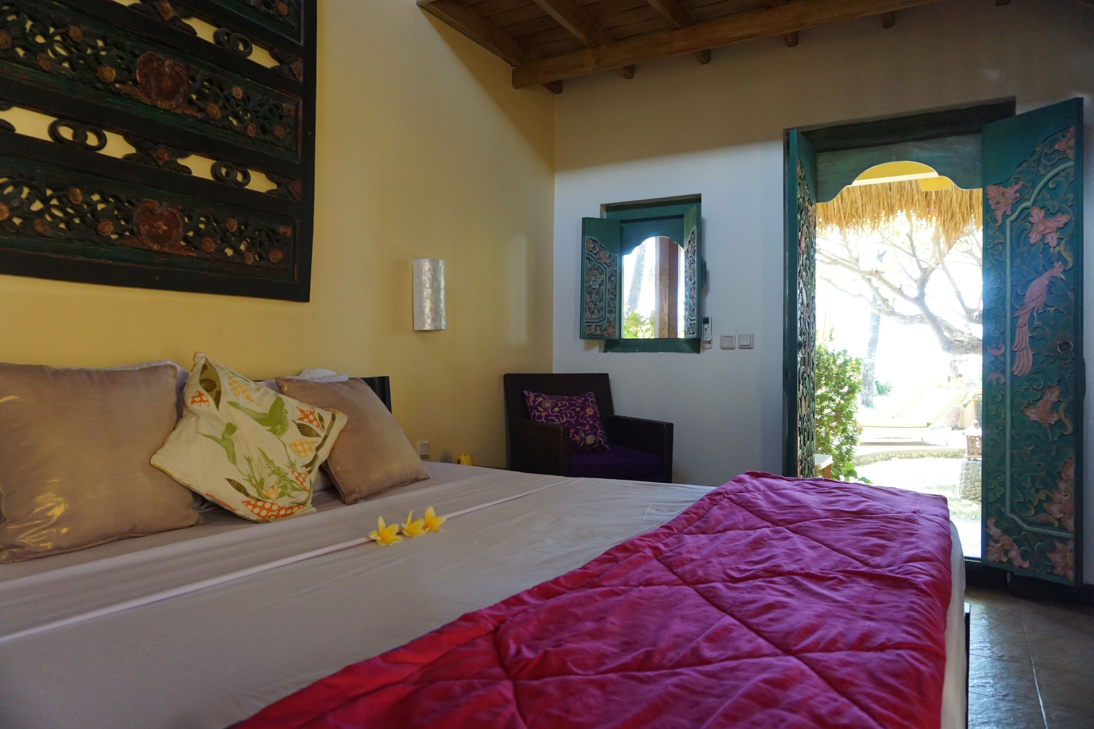 A neatly made bed with a red blanket, a wooden headboard, and decorative pillows.
