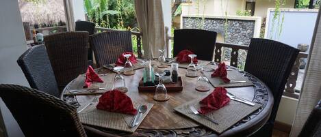 A round dining table set for six with wicker chairs, red napkins, and glassware.