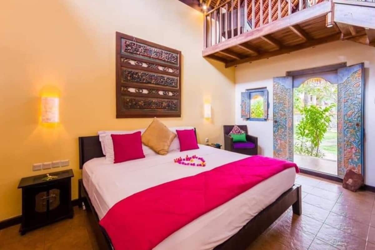 Quarto com cama grande, mesa de cabeceira, detalhe decorativo na parede e varanda com vista.