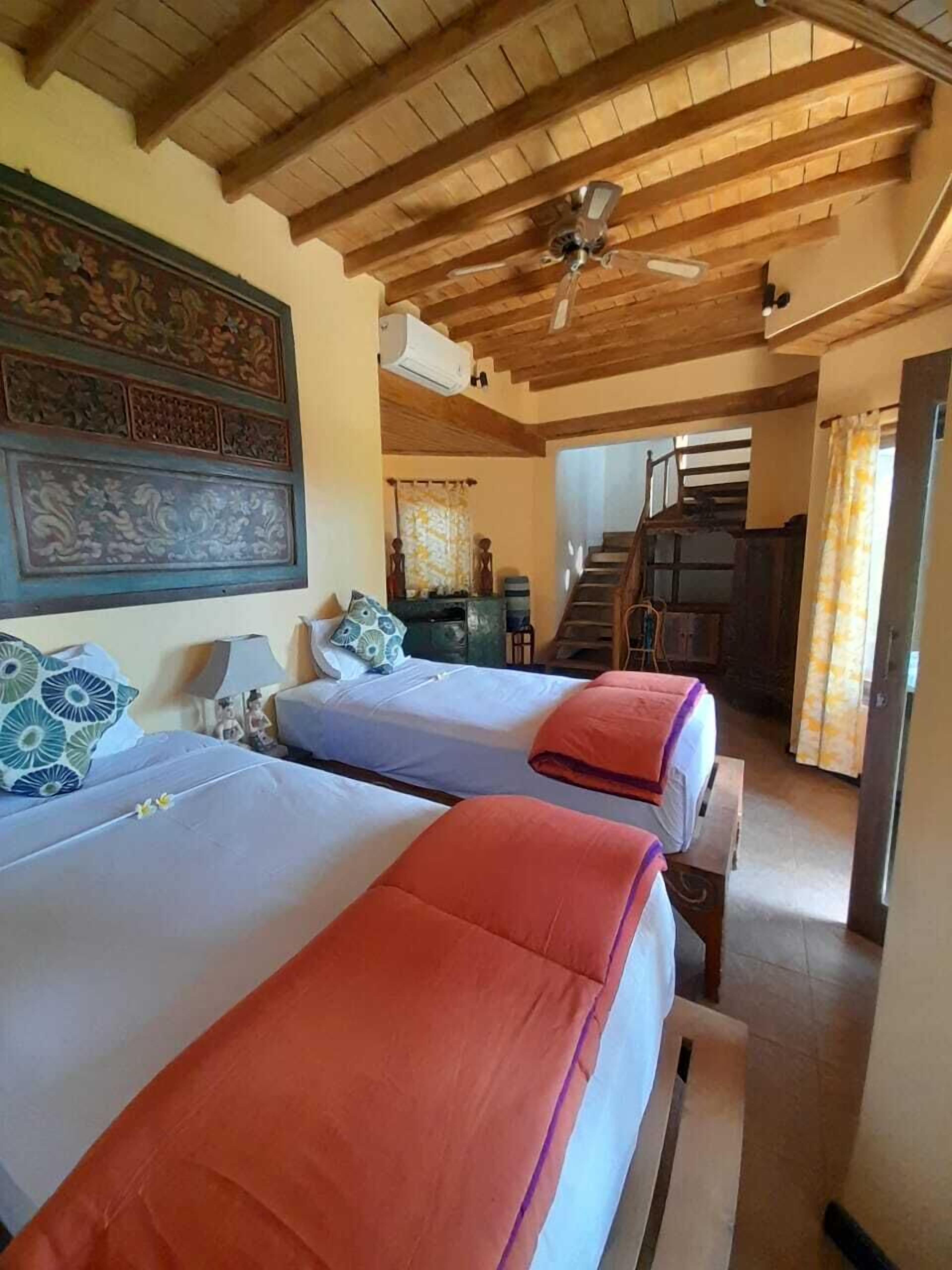 A hotel room with two beds, a ceiling fan, and a staircase leading to another area.