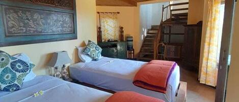 A hotel room with two beds, a ceiling fan, and a staircase leading to another area.