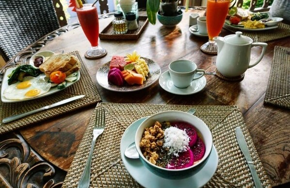 Un desayuno con diversos platos, una jarrón y una tetera sobre una mesa de madera.