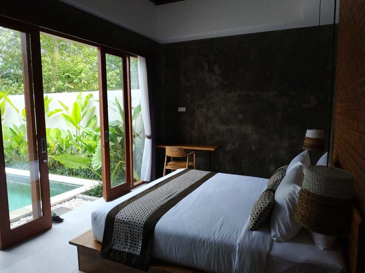 A bedroom with a bed, a desk, and a view of greenery outside.