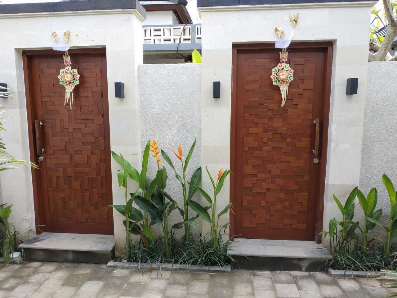 Two wooden doors with decorative elements, flanked by plants.
