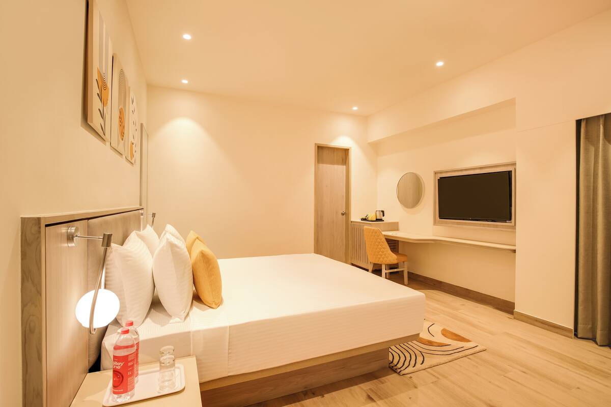 A modern hotel room with a bed, bedside table, and a desk with a chair.