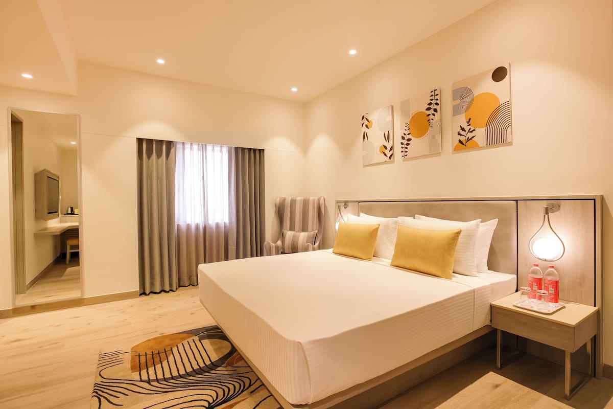 A modern hotel room with a large bed, a bedside table with a lamp, and artwork on the wall.