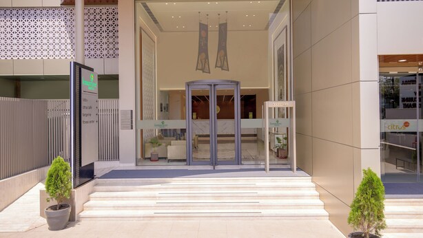 Una entrada moderna de edificio con puerta giratoria, plantas en macetas y un mostrador de recepción a la vista.