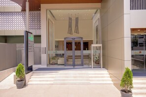 A modern building entrance with a revolving door, potted plants, and a visible reception area. - Lemon Tree Hotel Jamnagar (Jamnagar)