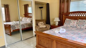 A bedroom with a large bed, a chair, a nightstand, and a mirror. - S3 BP| Steps to Beach | Save 15% if Book Non-Refundable (West Bay)