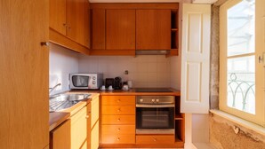 A compact kitchen with wooden cabinets, a microwave, a stove, and a window with a view.