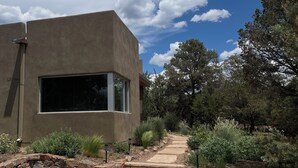 Un bâtiment moderne doté d’une grande fenêtre, d’un escalier en pierre menant à un sentier et entouré de verdure.