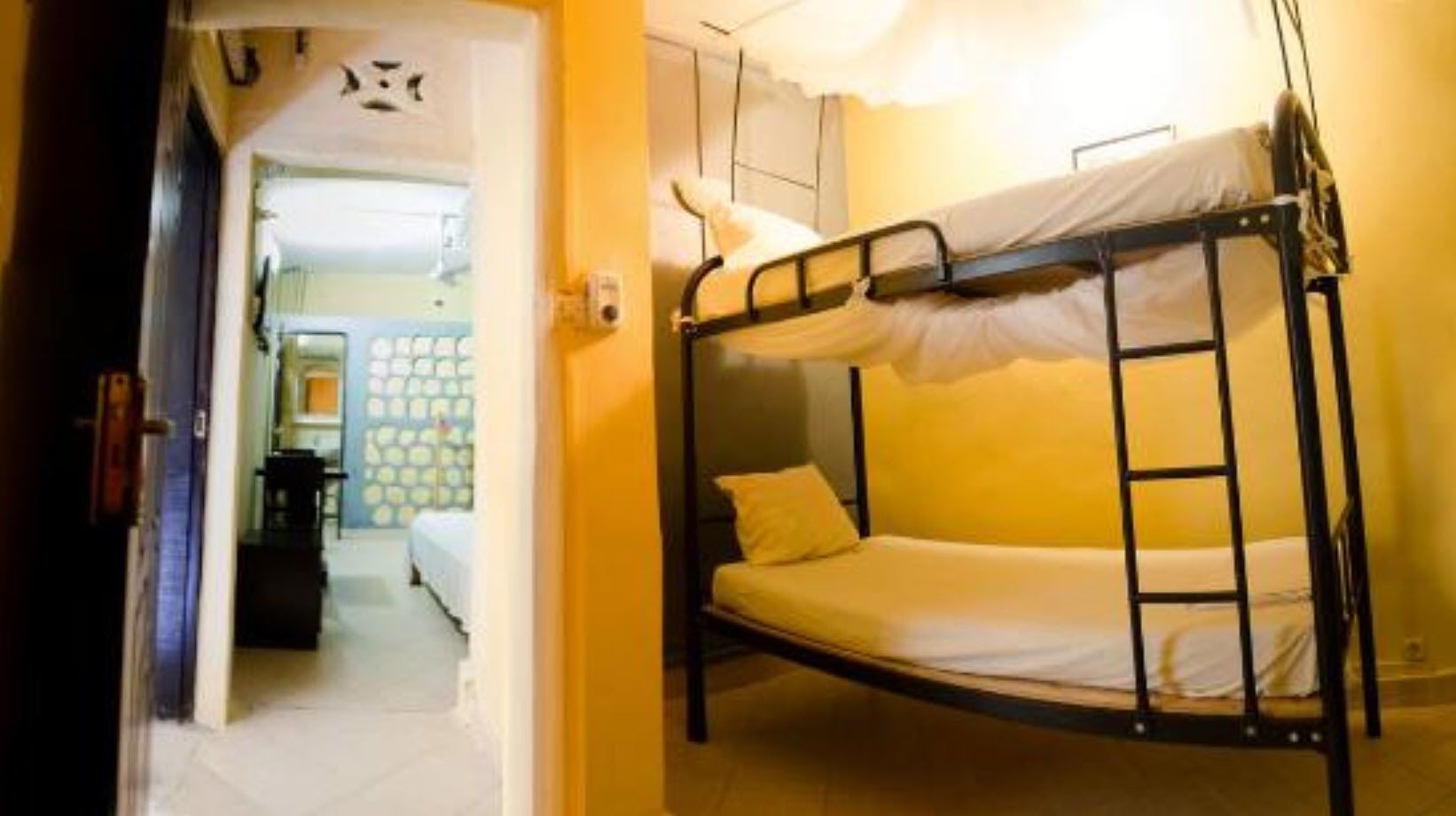 Una cama litera con escalera, una cama individual al fondo y una puerta que da a otra habitación.