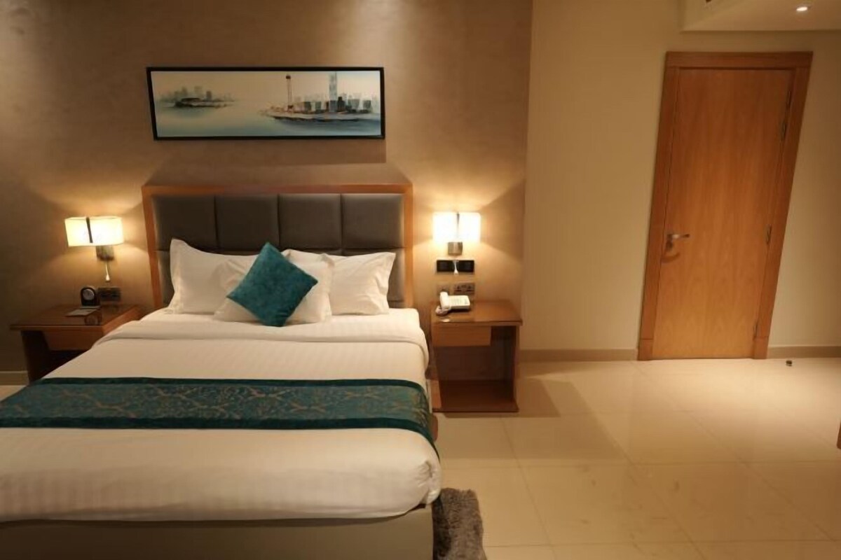 A hotel room with a bed, two bedside tables, a nightstand, a door, and a framed picture on the wall.