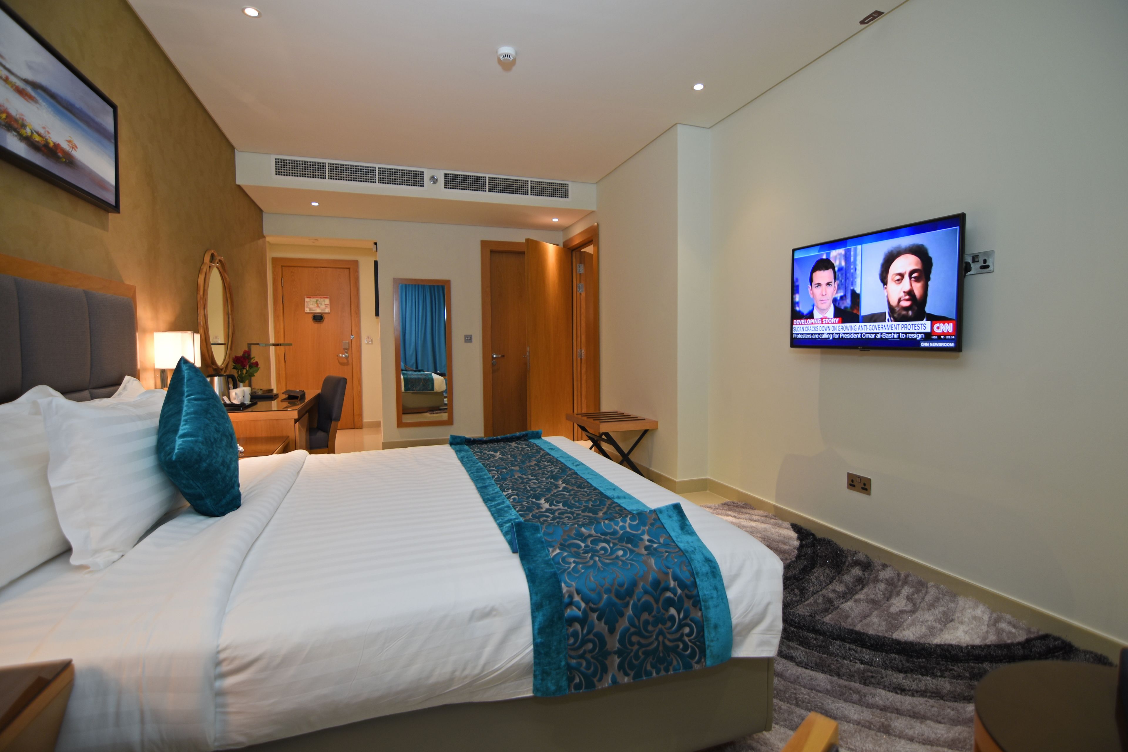 A hotel room with a large bed, a TV mounted on the wall, a desk, and a chair.