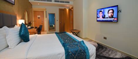 A hotel room with a large bed, a TV mounted on the wall, a desk, and a chair.