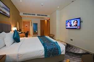 Una habitación de hotel con una cama grande, un televisor en la pared, un escritorio y una silla.