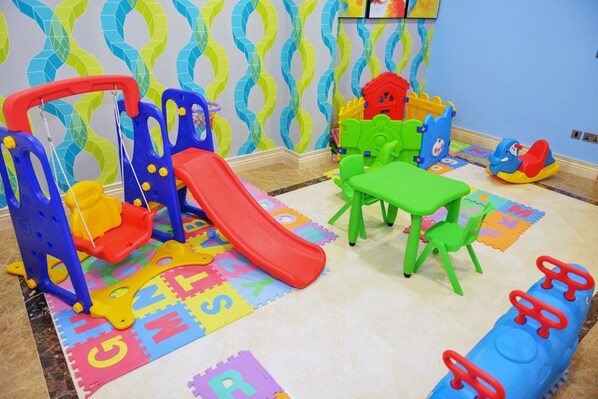 A play area with a slide, play structures, and alphabet foam mats on the floor.