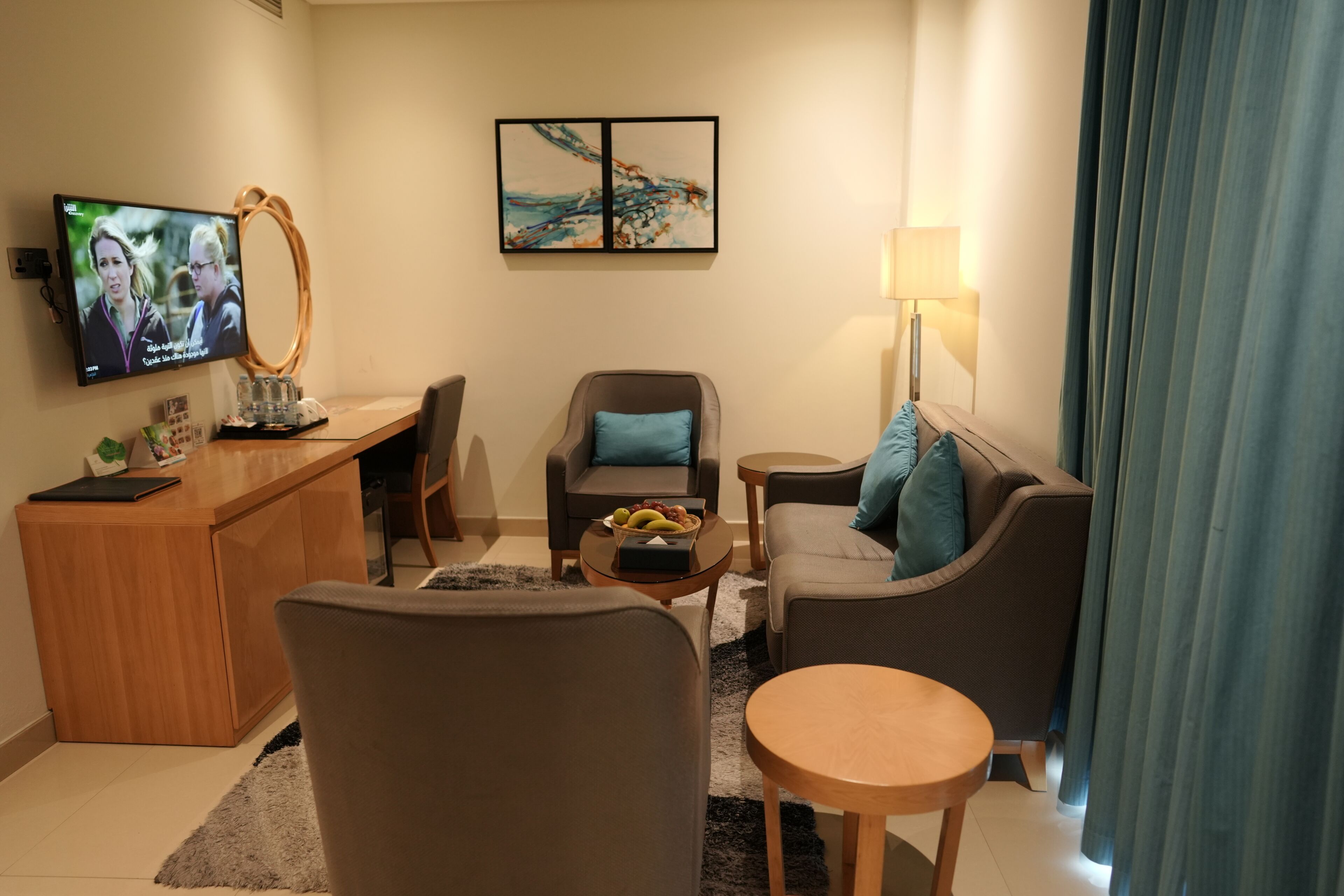 Ein Hotelzimmer mit einem Holztisch, einem Fernseher, einem Sofa, einem Sessel und einer Lampe.