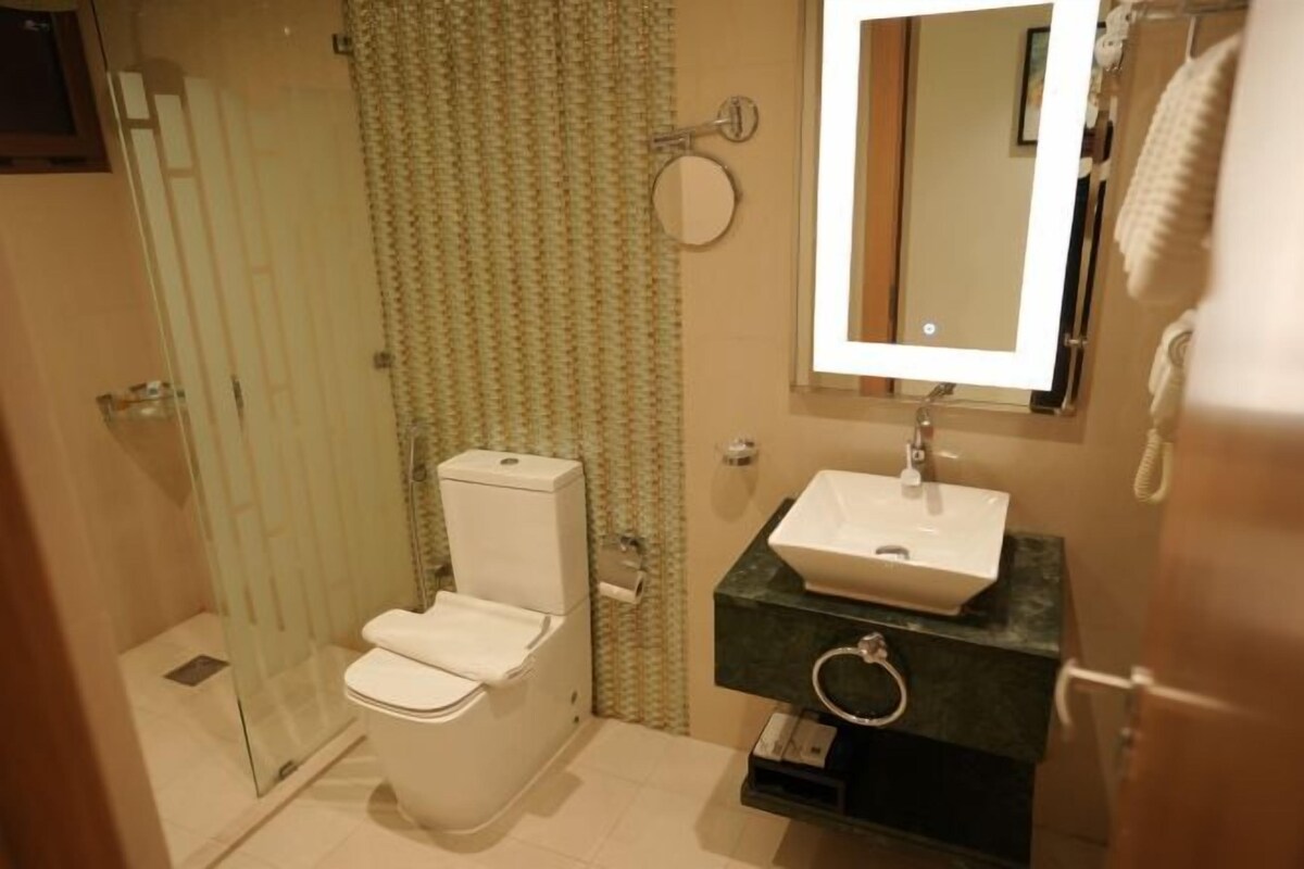 A bathroom with a toilet, a sink, a mirror, and a shower area.