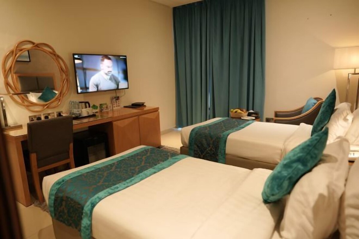 A hotel room with two beds, a desk, a chair, a television, and a large window with curtains.