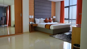 Una habitación de hotel moderna con una cama grande, un armario, una mesita de noche y un amplio ventanal con cortinas.